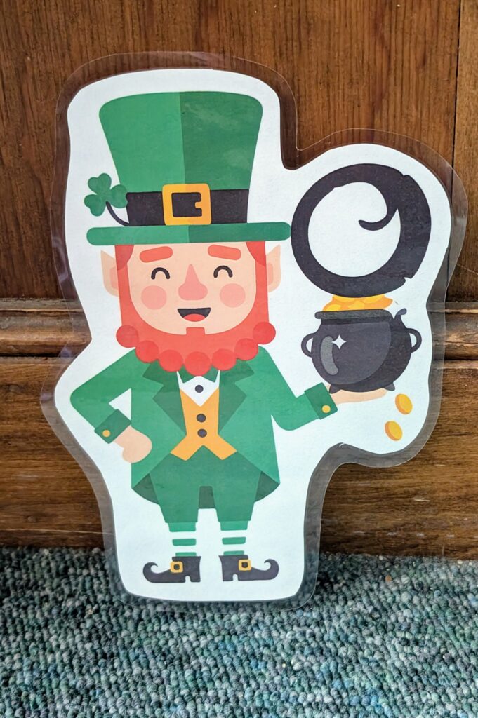 The photo shows a paper cut out of a merry looking leprechaun holding the letter O.