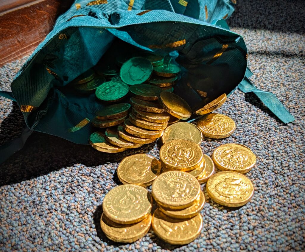 Photo shows a close up of gold chocolate coins flowing out of a green sack.