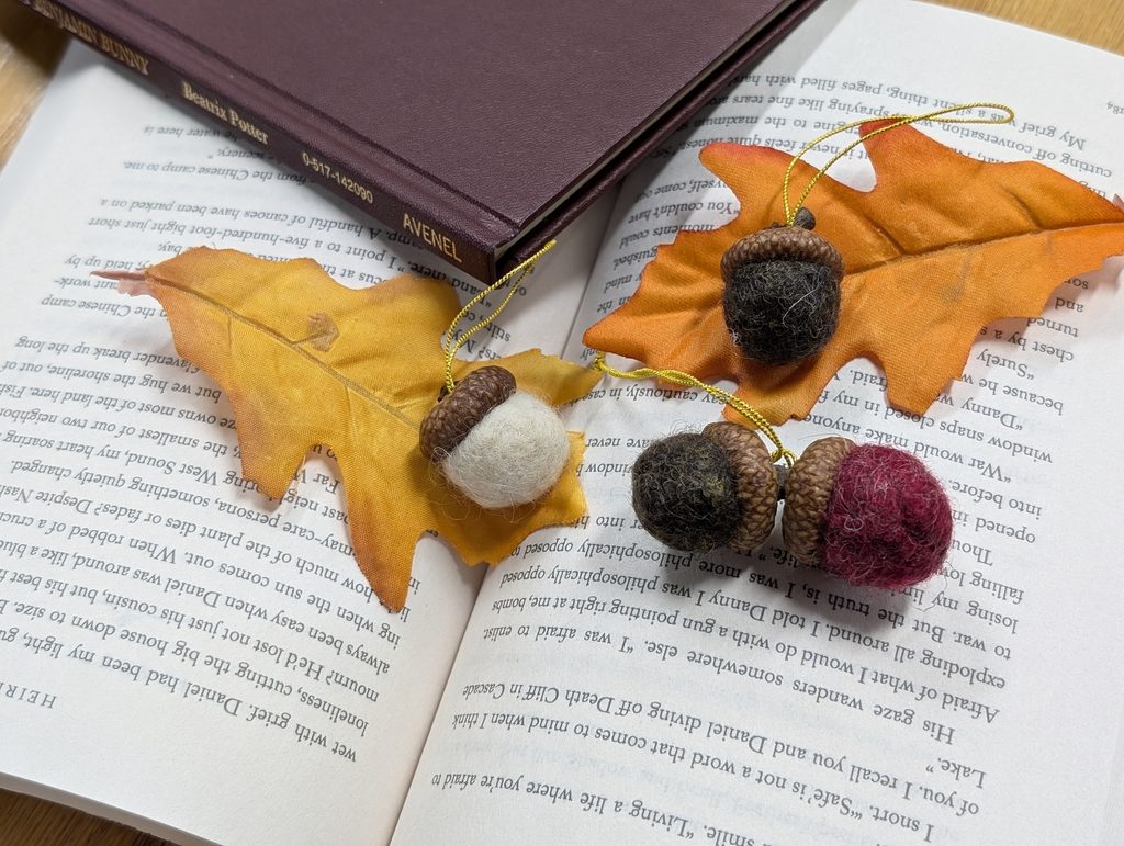 Several hand-crafted acorn decorations crafted out of wet-felted wool are displayed on top of an open book, to demonstrate what Friday's craft will be.